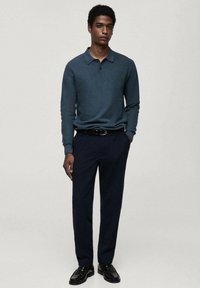 Námořnické modré kalhoty spárované s tmavě tyrkysovou polokošilí s dlouhým rukávem. Hladká textura, přiléhavý střih a černý pás s stříbrnou sponou.