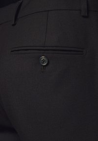 Czarne spodnie z tkaniny o fakturowanej powierzchni, wyposażone w tylnią kieszeń zapinaną na okrągły guzik oraz mały ozdobny ścieg.