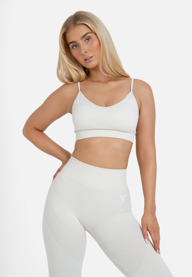 Weißer Sport-BH mit dünnen Trägern und geripptem Design, kombiniert mit hochtaillierten, figurbetonten Leggings mit strukturierten Paneelen und Logo-Detail.