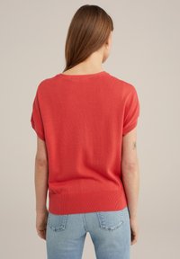 Krótki rękaw, koralowy sweter dzianinowy z okrągłym dekoltem i prążkowanym wykończeniem u dołu. Tył ma gładką teksturę oraz subtelne szwy na ramionach.