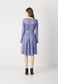 Abito lilac a maniche lunghe con dettagli arricciati, vita legata e schiena a chiave. Tessuto liscio, gonna fluida e corpo ben aderente.
