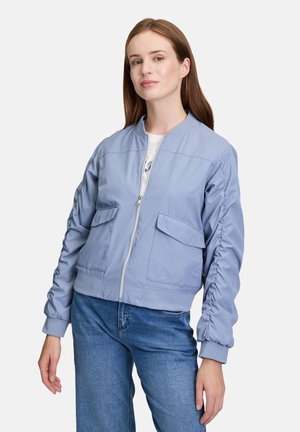 Veste bomber bleu clair avec zip sur le devant, poignets côtelés et deux poches avant, dotée d'une texture de tissu lisse.