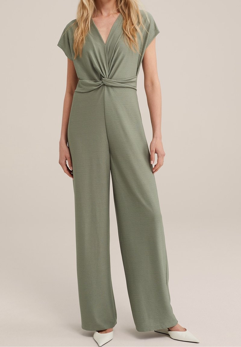 Combinaison vert olive avec un col en V profond et un détail torsadé à l'avant. Fabriquée en tissu doux et texturé, avec des jambes larges et des manches courtes.