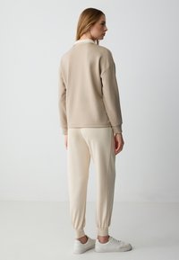 Beige sweater met een relaxte pasvorm en ribgebreide manchetten, gecombineerd met crèmekleurige tapered broeken, met elastische enkels en witte sneakers.