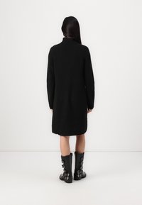 Black knitted dress with a high neckline, long sleeves, and a loose fit, paired with knee-high black boots featuring buckle accents.