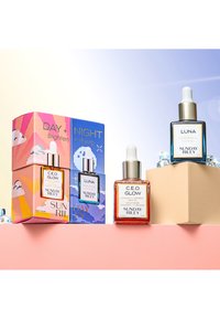 Deux flacons de sérum sur un fond pastel. L'un présente un compte-gouttes en verre transparent et un capuchon en métal argenté ; l'autre, un flacon en verre orange avec un capuchon similaire. L'emballage est coloré de manière vive avec des motifs géométriques et du texte indiquant "C.E.O. GLOW" et "LUNA."
