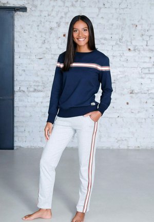 Marineblauer Sweatshirt mit horizontalen roten und weißen Streifen, kombiniert mit hellgrauen Jogginghosen, die rote und weiße Seitenstreifen aufweisen.