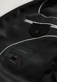 Black satin interior with tailored fit tag, featuring intricate subtle pattern and contrasting white accents. Includes a black button closure.