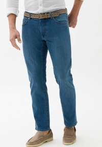 Jeans in denim blu con una vestibilità slim, dotati di una cintura intrecciata beige. Il tessuto ha una texture liscia e dettagli di leggera scoloritura.
