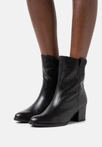 Zwarte leren enkellaarzen met een puntige neus, gestructureerde afwerking en een gematigde blokhak. Voorzien van zij-elastische panelen voor eenvoudig aan- en uittrekken.