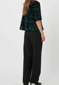 Top in sequins turchesi con maniche corte, design a peplo, abbinato a pantaloni a vita alta neri con gamba larga. Tessuto morbido e accenti lucenti.