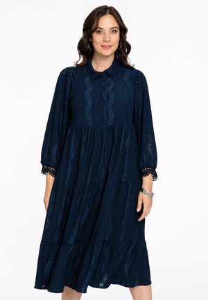 Navy blauwe gelaagde jurk van textuurstof met een kraag, knoopjes aan de voorkant en kantaccenten op de mouwen. Bevat golvende uitsnijpatronen.