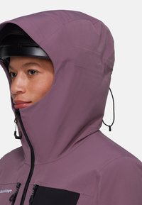 Lila wasserdichte Jacke mit hohem Kragen, verstellbarem Kapuzen und schwarzen Reißverschlusstaschen. Glatte Textur und minimalistisches Design.
