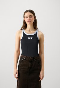 Svart ribbad linne med vit kant och grafik av solglasögon på bröstet, kombinerat med en högmidjad mörkbrun denimkjol.