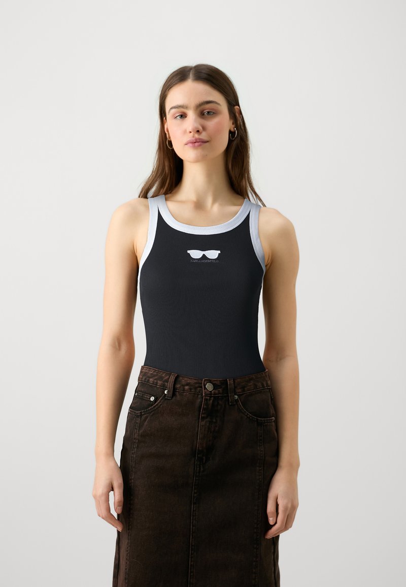 Svart ribbad linne med vit kant och grafik av solglasögon på bröstet, kombinerat med en högmidjad mörkbrun denimkjol.