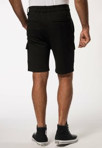 Schwarze Cargo-Shorts mit elastischem Bund, ausgestattet mit zwei Gesäßtaschen und einer seitlichen Utility-Tasche, kombiniert mit schwarzen High-Top-Sneakern.