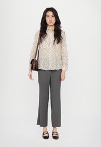 Sheer, printed blouse with a button-up design, paired with gray, wide-leg trousers. Black, flat shoes with double strap accents.