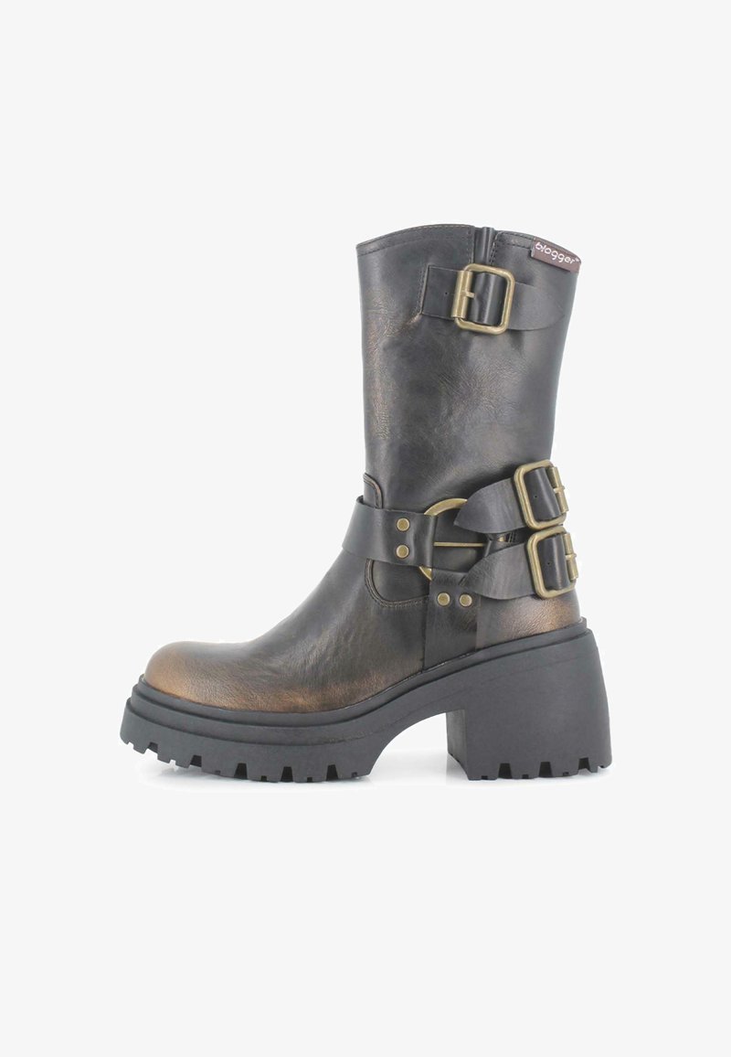 Bota de cuero negro hasta la rodilla con acentos metálicos, suela de goma gruesa y dos hebillas laterales. Presenta una puntera redonda y acabado texturizado.