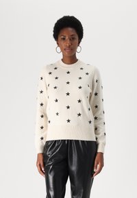 Pull en tricot crème avec des motifs d'étoiles noires, col et poignets côtelés. Associé à un pantalon en cuir noir.