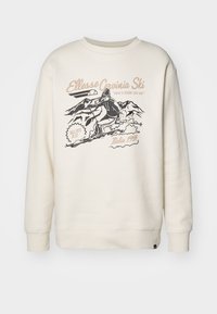 Sudadera color crema con un estampado gráfico de un esquiador y montañas. Tiene un cuello redondo, puños acanalados y un corte holgado.