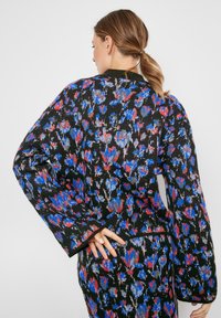 Strickjacke mit schwarzem Grund und einem mehrfarbigen Blumenmuster in Rot, Blau und Grau, langen Ärmeln und einer lockeren Passform.