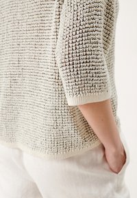 Jasnobeżowy sweter o teksturowanej fakturze, luźny krój, z małym ściętym dekoltem i rękawami ¾. Miękka, dziana tkanina, casualowy styl.