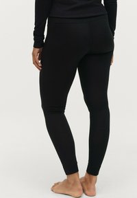 Zwarte leggings van rekbaar materiaal, met een aansluitend ontwerp, naadloze zijkanten en enkel-lengte boorden. Blote voeten weergegeven.