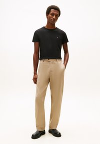 Črna bombažna majica, bež krojene hlače in črni čevlji. Model s pravim krojem in gladko teksturo. Gumb detajl na pasu.