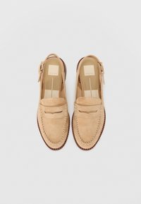 Bež nubuk loafers s šivanim uzorkom, otvorenom petom i podesivom kopčom. Imaju teksturiranu potplatu i glatku unutrašnjost.