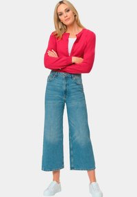 Rode gebreide cardigan met knoopdetails, gecombineerd met hooggewijze, wijde blauwe jeans en witte sneakers. Gestructureerd brei- en denimmerk.