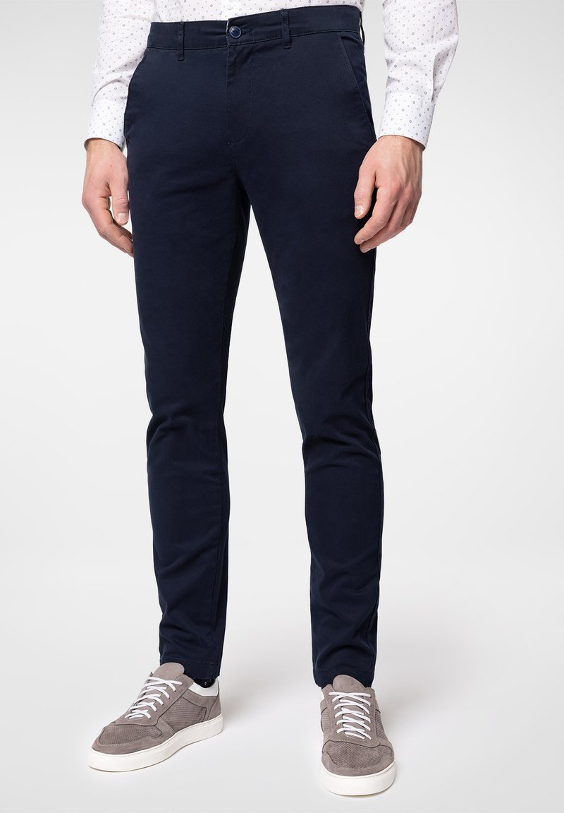 Nadmorskie niebieskie chinosy wykonane z mieszanki bawełny, z dopasowanym krojem, płaskim przodem oraz kieszeniami z boku i z tyłu. W połączeniu z szarymi trampkami.