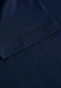 Námořnická modrá košile s krátkým rukávem, hladkou texturou a čistými švy, která ukazuje okraj rukávu a tělo oděvu.