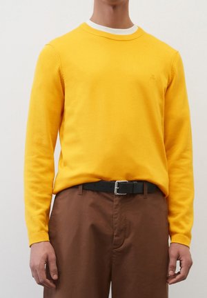 Pull en tricot jaune avec un col rond blanc et des manches longues, associé à un pantalon marron avec une ceinture noire. Texture lisse.