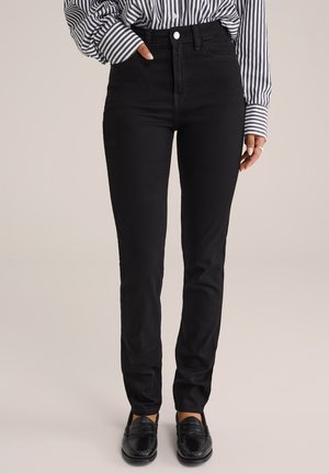 Černé džíny s vysokým pasem a slim fit, vyrobené z denimu. Mají zapínání na předním knoflíku a zadní kapsy. Nosené s pruhovanou košilí.