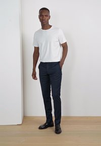 Camiseta blanca de manga corta combinada con pantalones ajustados azul marino y mocasines negros brillantes, sobre un suelo de madera clara frente a un fondo neutro.