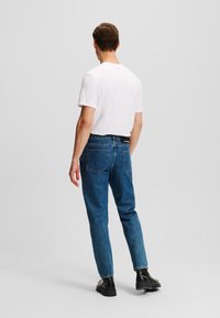 Modré denimové džínsy s voľným strihom, dizajnom s piatimi vreckami a kontrastným prešívaním, skombinované s jednoduchým bielym tričkom s krátkym rukávom.