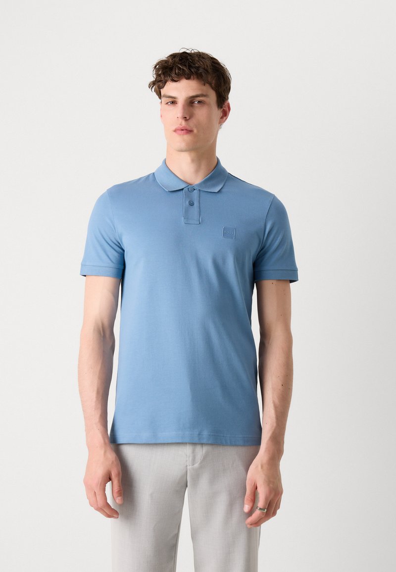 Camisa polo azul claro de manga corta, con diseño de cuello y un pequeño logo en el pecho. Material de algodón suave y liso.