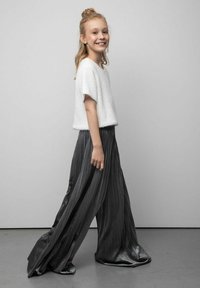 Biały teksturowany top z krótkim rękawem zestawiony z wysokim stanem, plisowanymi szarymi spodniami o płynnym kroju i delikatnym połysku.