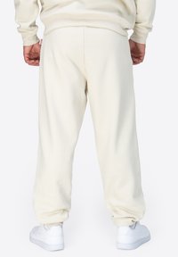 Ljusbeige sweatpants med avslappnad passform, muddar vid anklarna och justerbar midja. Matchade med vita sneakers. Slät textur, minimalistisk design.