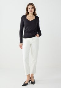 Haut à manches longues noir avec un décolleté en V, associé à un pantalon blanc à longueur de cheville et des escarpins noirs à bout pointu. Textures de tissu lisses.