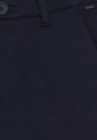 Granatowe materiałowe spodnie o gładkiej fakturze, z zapięciem na guzik i subtelnymi detalami w postaci przeszyć. Minimalistyczny design bez widocznych wzorów.