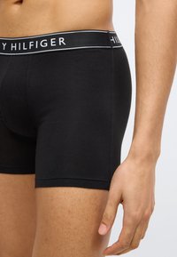 Μαύρα βαμβακερά boxer briefs με μαύρη ζώνη μέσης που απεικονίζει το λευκό λογότυπο "TOMMY HILFIGER". Ομαλή υφή, εφαρμοστή σχεδίαση με κοντά πόδια.