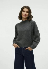 Gray knitted sweater with a high neckline, long puffed sleeves, and a relaxed fit, paired with dark denim jeans featuring a button closure.