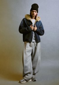Jeansjacka med pälsliknande krage, grå sweatshirt och överdimensionerade gråa sweatpants. Svart mössa och grå sneakers fullända looken.
