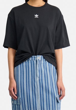 Person wearing a black Adidas t-shirt tucked slightly into a high-waisted blue and white vertical striped skirt with cargo pockets.