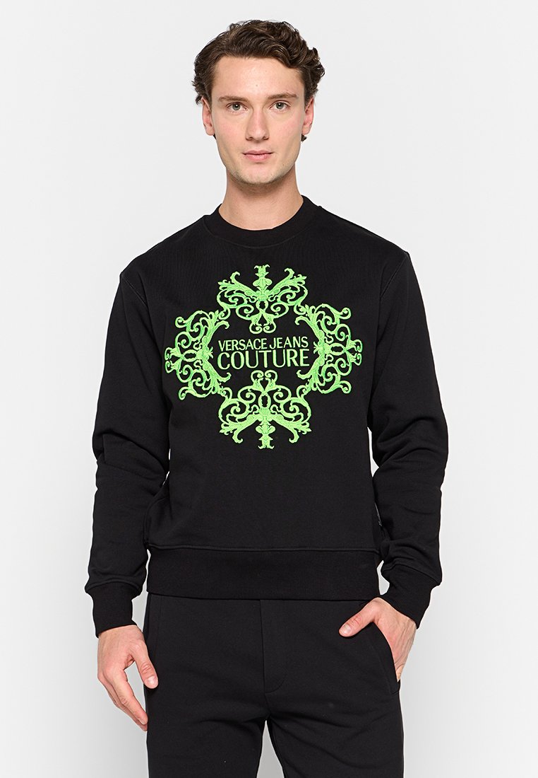 Sudadera negra con un gran gráfico verde ornamentado y el texto "VERSACE JEANS COUTURE" en el centro, cuello redondo y puños acanalados.