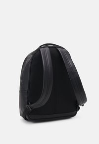 Zaino nero con schienale in rete, spallacci imbottiti e dettagli in pelle liscia. Presenta una forma arrotondata e chiusura con zip.