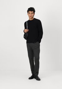 Schwarzer Pullover, graue Hose und schwarze Knöchelstiefel. Schwarze Umhängetasche mit weißem "Hugo" Textband. Lässiger Sitz, glatte Textur.