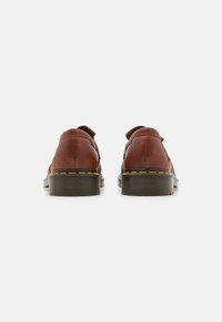 Ruskeat nahkakengät, joissa on teksturoitu pinta, kestävä kumipohja, erottuva keltainen tikkaus ja klassinen loafer-muotoilu.