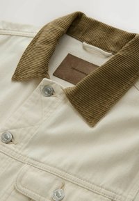 Beige denimjakke med brun fløjlskrave, sølvfarvede trykknapper og et lædermærke. Tekstureret stof og kontrastfuldt kravedesign.